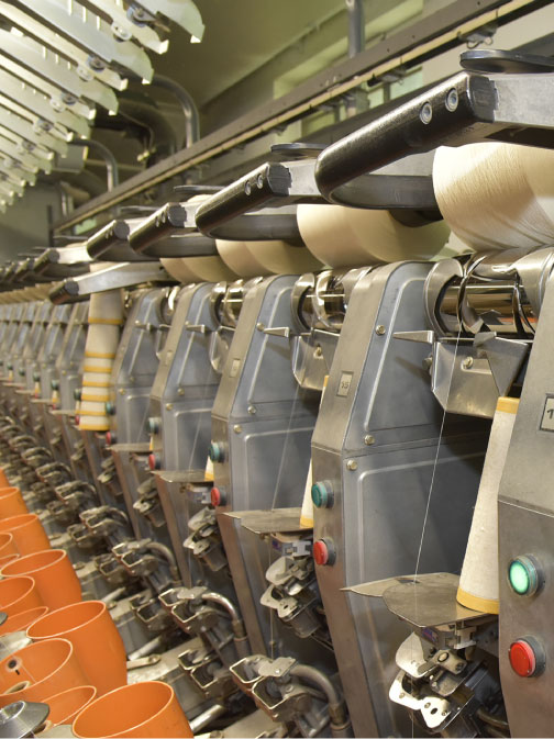 Dettaglio tecnico di macchinari per la ritorcitura industriale con rocche di cotone in lavorazione.