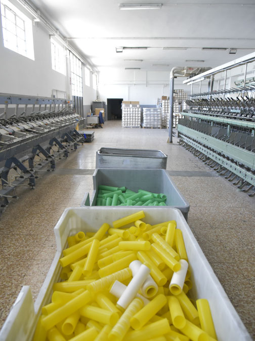 Ampia area interna dello stabilimento con contenitori di tubetti colorati per la raccolta e il riciclo del filato.